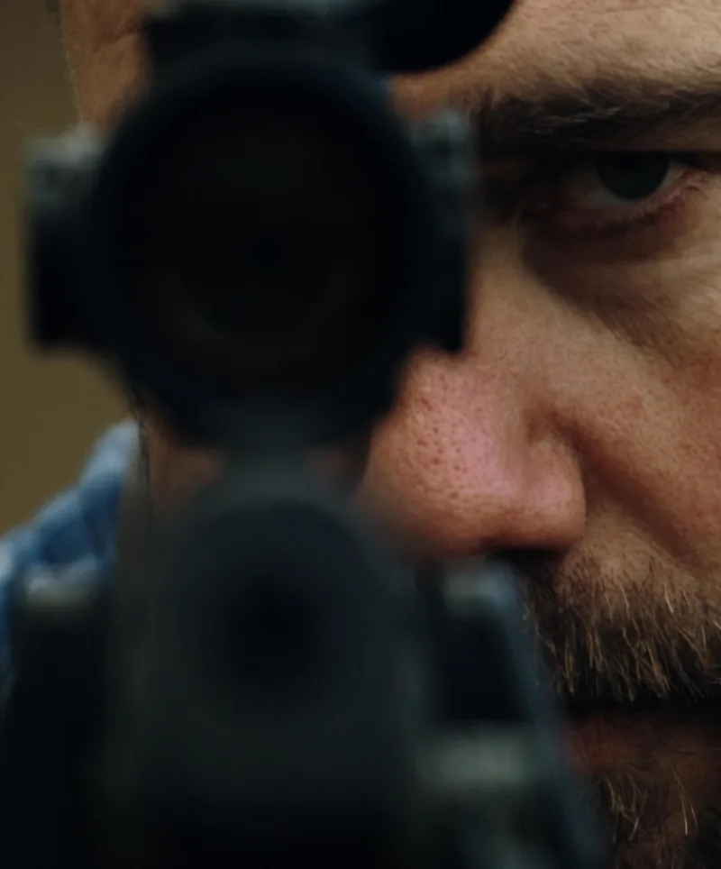 Close-up of a rifle scope with Ryan behind the glass
